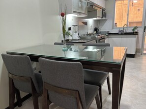 A modern kitchen with a glass dining table, grey upholstered chairs, and a stainless steel stove. - Cala Cala Apartment (Cochabamba)