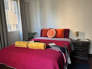 A hotel room with a large bed, a nightstand, a lamp, and a window with curtains. - Cala Cala Apartment (Cochabamba)