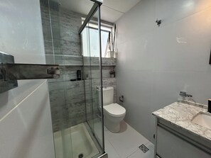Ein modernes Badezimmer mit Duschkabine aus Glas, Toilette und Waschtisch mit Marmorplatte.