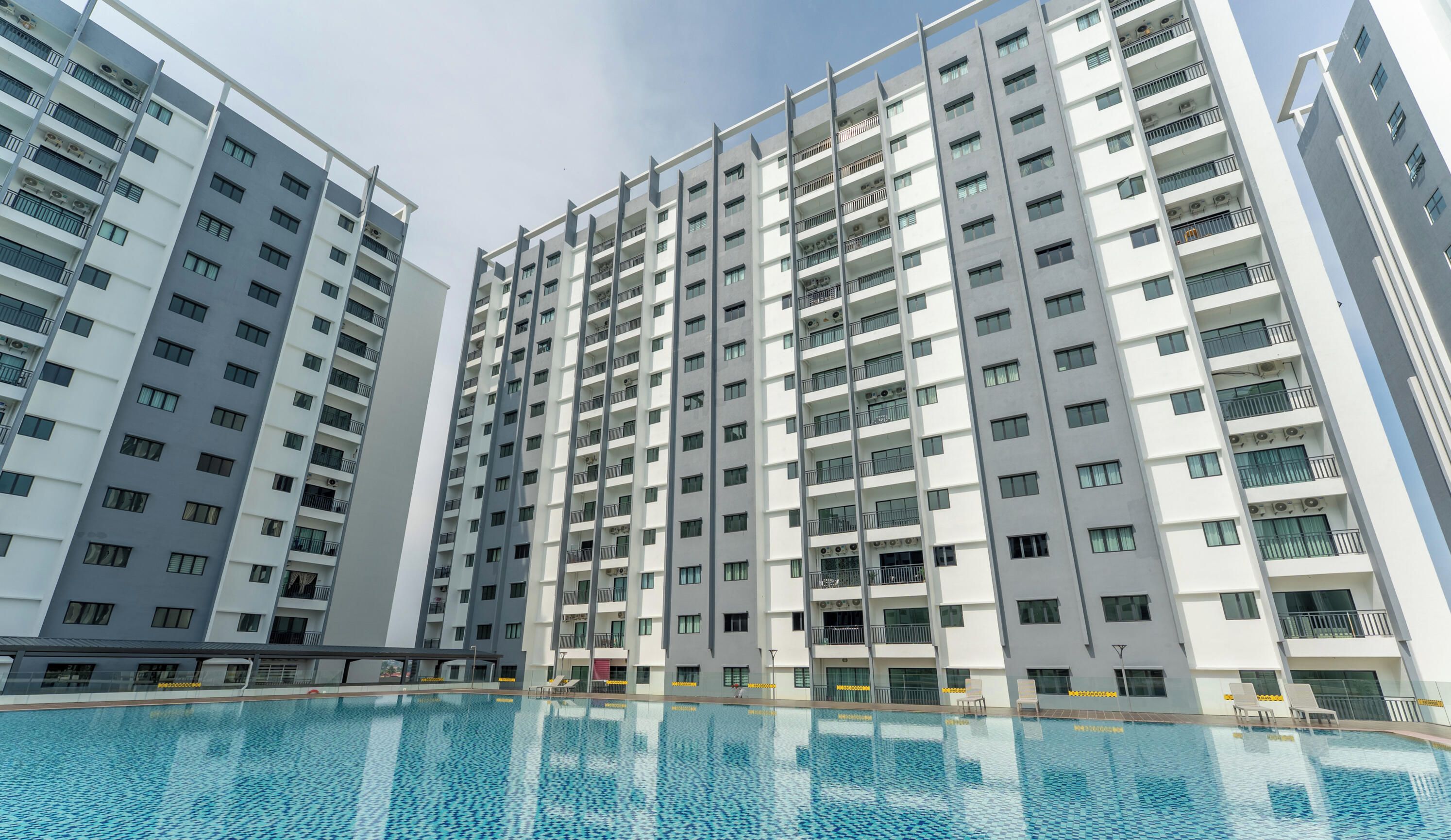 A high-rise residential building with multiple balconies, a swimming pool, and a clear sky.