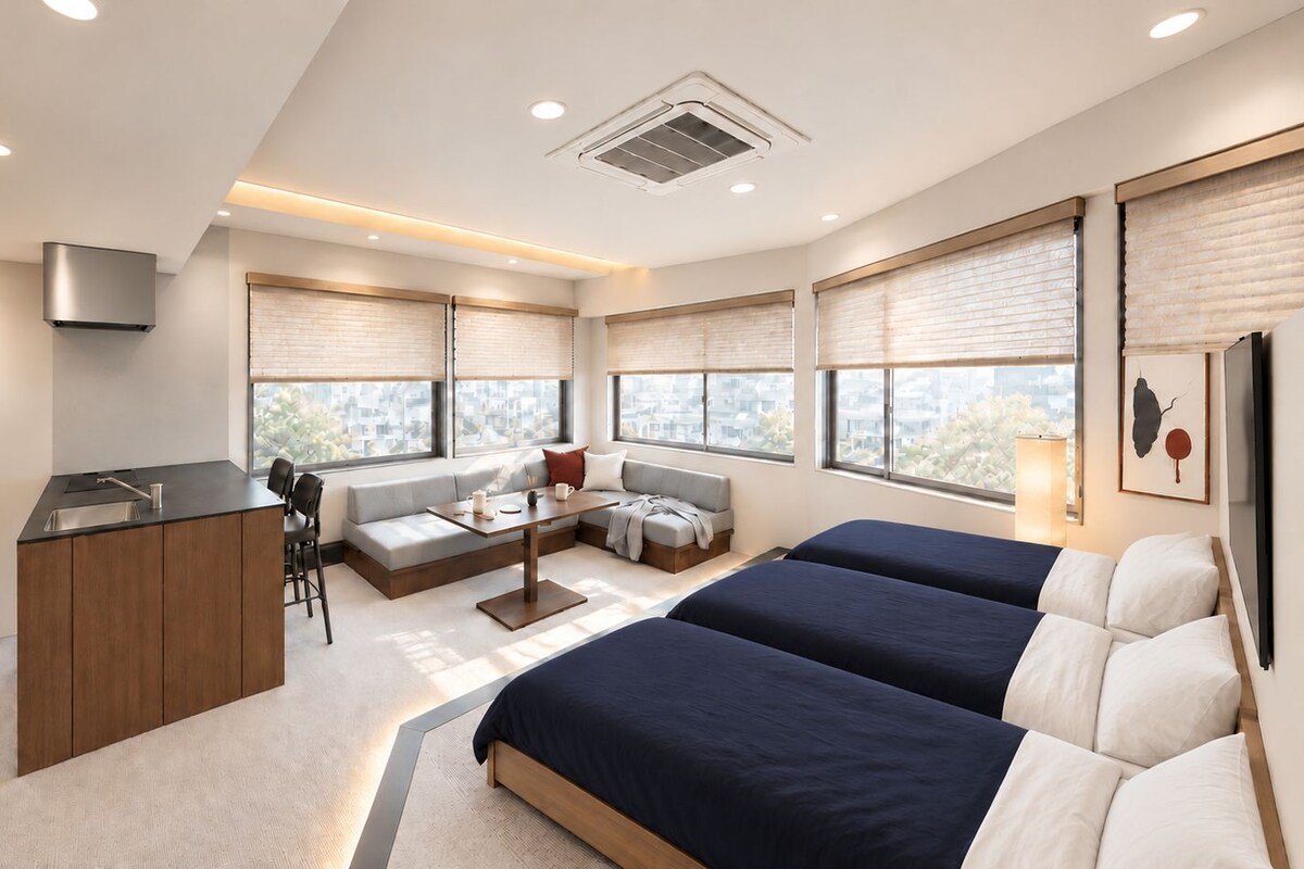 A modern hotel room with a kitchenette, a seating area with a sofa and chairs, two beds, large windows with blinds, and a ceiling vent.