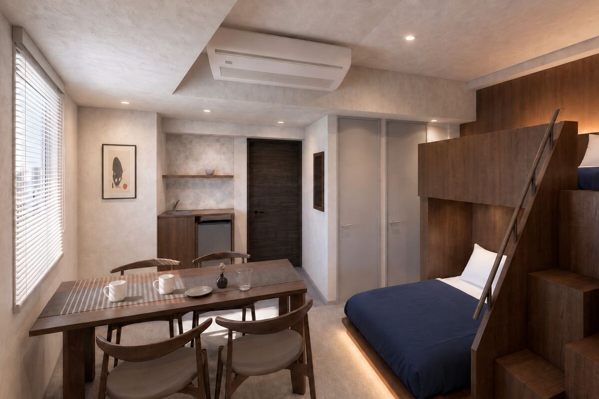 A compact bedroom with a bunk bed, a dining area with a table and chairs, and a kitchenette.