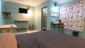 Un dormitorio con cama, mesita de noche y televisor montado en la pared.