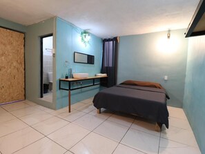 A bedroom with a bed, a bedside table, a mirror, and a window with curtains.
