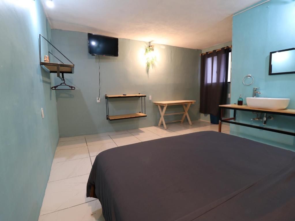 A bedroom with a bed, a TV mounted on the wall, a bedside table, a mirror, and a window with curtains.