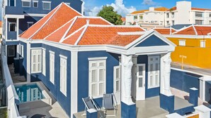 A blue building with white shutters, a swimming pool, and a small patio with chairs. - Vrbo Property (Willemstad)