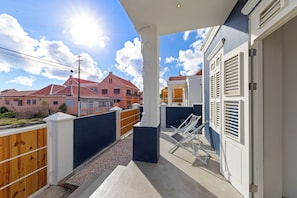 Ein Balkon mit Blick auf angrenzende Häuser, einem Holzzaun und einer weißen Tür.