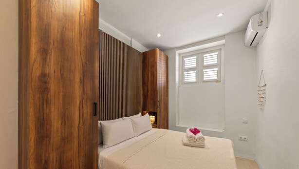 A bedroom with a bed, wooden paneling, a window with blinds, and an air conditioning unit. - Vrbo Property (Willemstad)