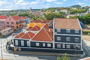 A multi-story building with a dark facade and red-tiled roofs, featuring a prominent entrance with a sign. - Kas Leon | 6-person villa in Otrobanda (Willemstad)