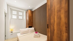 A bedroom with a bed, a bedside lamp, a wooden wardrobe, and a window with blinds. - Vrbo Property (Willemstad)