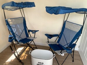 Two portable camping chairs with attached umbrellas, a white bucket labeled 'COLD DRINK,' and a wooden floor. - Atlantic Breeze Getaway with Pool (Atlantic Breeze)