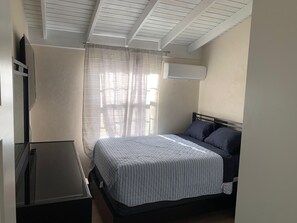 A bedroom with a bed, a nightstand, a TV, and a window with curtains. - Atlantic Breeze Getaway with Pool (Atlantic Breeze)