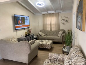 A living room with a sofa, armchair, and ottoman, a television mounted on the wall, and a ceiling fan. - Atlantic Breeze Getaway with Pool (Atlantic Breeze)