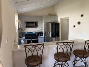 A modern kitchen with stainless steel appliances, a central island with bar stools, and a dining area with a table and chairs. - Atlantic Breeze Getaway with Pool (Atlantic Breeze)
