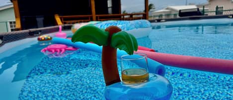 A swimming pool with inflatable toys and a glass of liquid.