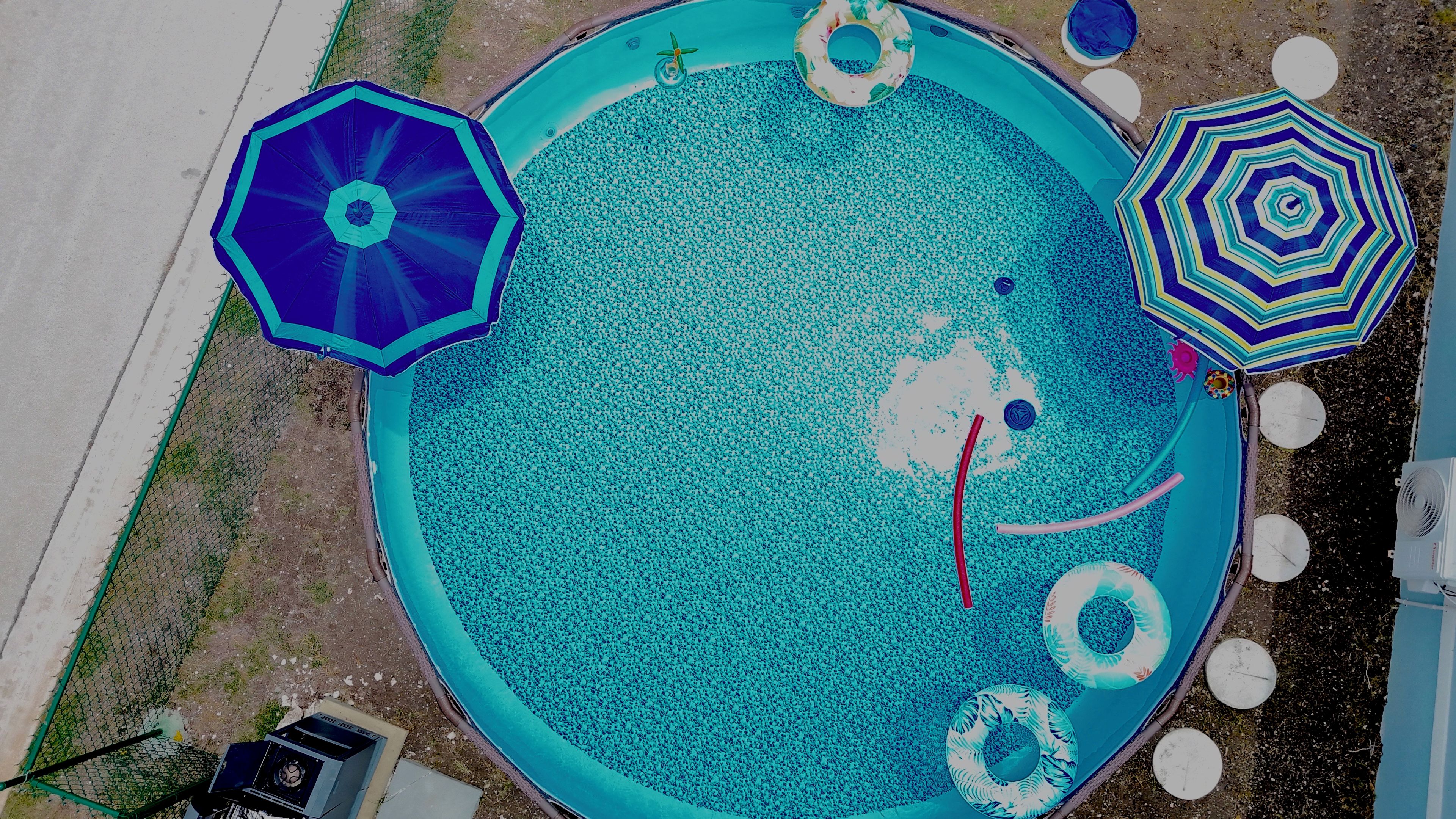 A circular pool with a surrounding fence, a water filtration system, and multiple water toys.