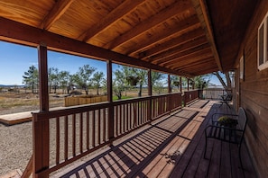 Eine überdachte Holzterrasse mit Geländer, einer Bank und einem Blumentopf.