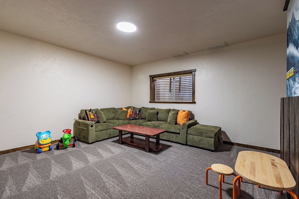 Una habitación con un sofá seccional verde, una mesa de centro de madera, una mesita de madera y dos sillas.