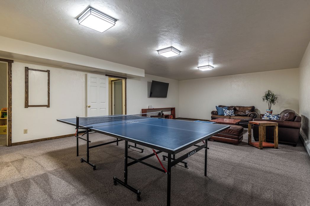A room with a ping pong table, a sofa, a small table, and a television mounted on the wall.