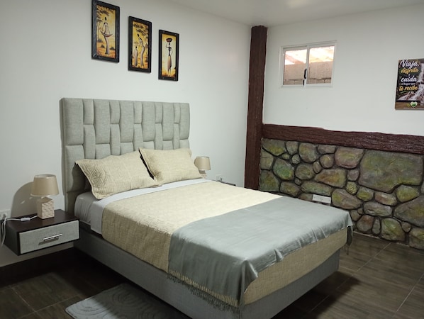 A bedroom with a bed, bedside tables, a lamp, a stone wall, and artwork on the wall.
