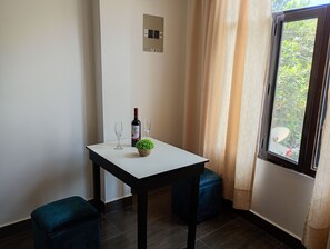 Een kleine kamer met een witte tafel, twee stoelen, een fles wijn en een bloempot.