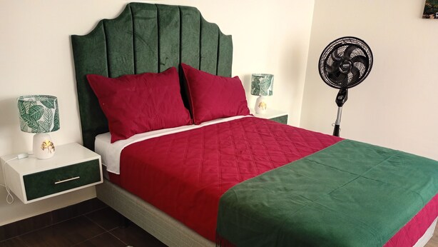 A bed with a green headboard, red and green bedding, a bedside table with a lamp, and a floor lamp. - An Airbnb-style vacation rental, perfect if you're visiting Podocarpus Park. (Zamora)