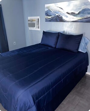 A bed with a dark blue bedspread and pillows, a wall-mounted air conditioning unit, and a painting of a mountainous landscape. - 3-bedroom mobile home in beautiful Eagle Pass with AC (Eagle Pass)