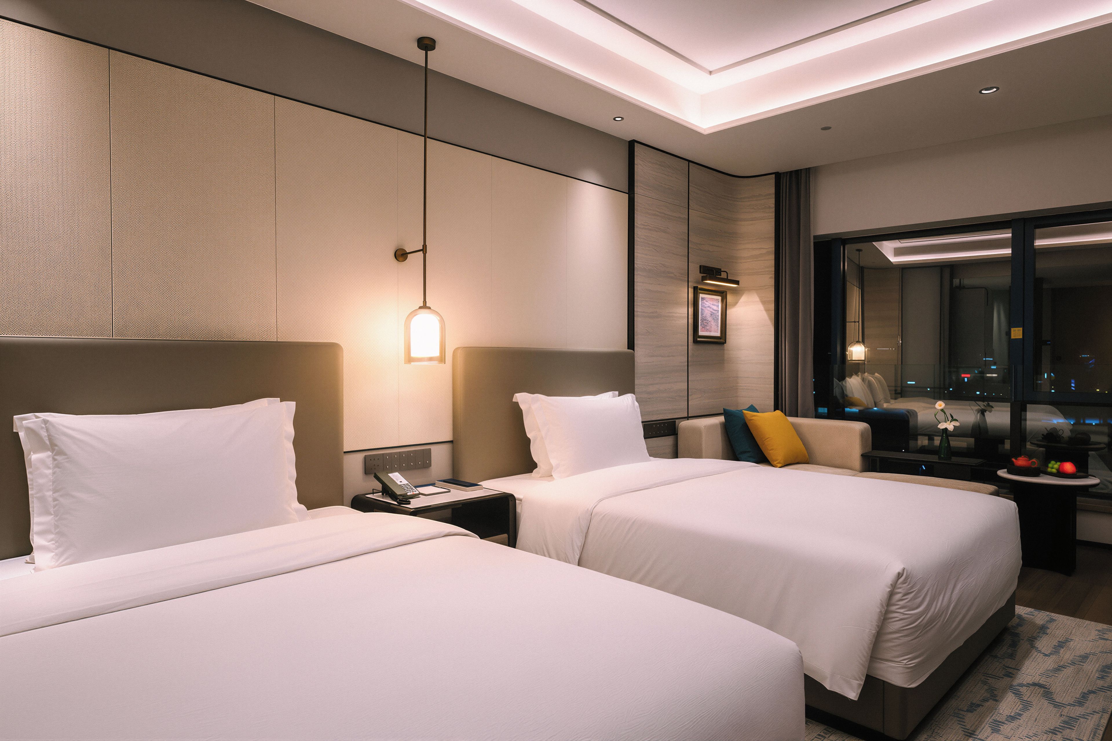 A hotel room with two beds, a desk, a mirror, and a view of the city.
