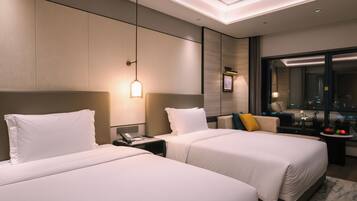 A hotel room with two beds, a desk, a mirror, and a view of the city.