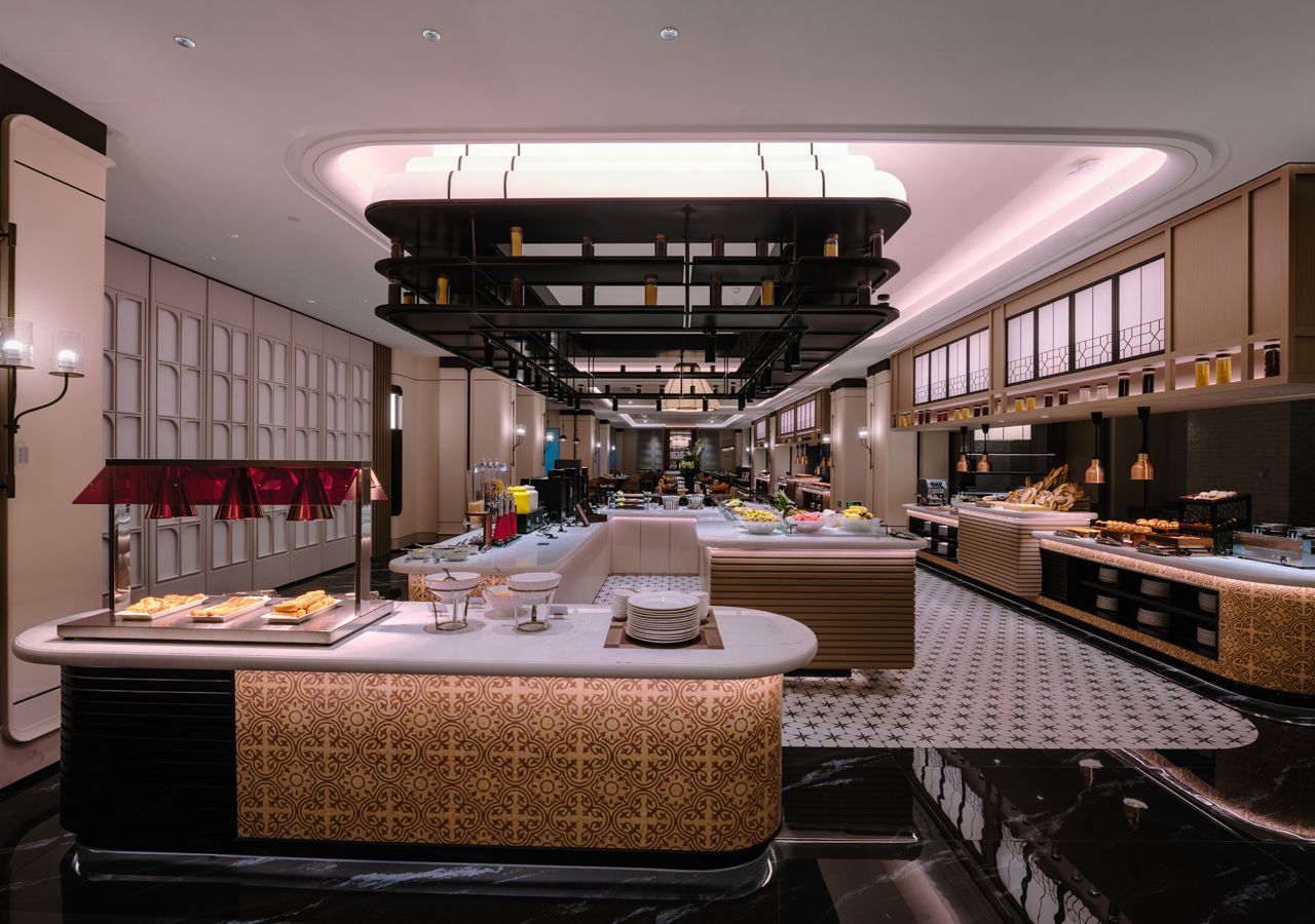 A modern hotel lobby with a central seating area, a reception desk, and a buffet setup.