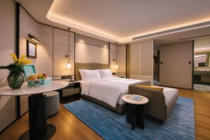 A modern hotel room with a bed, bedside table, and a small seating area.