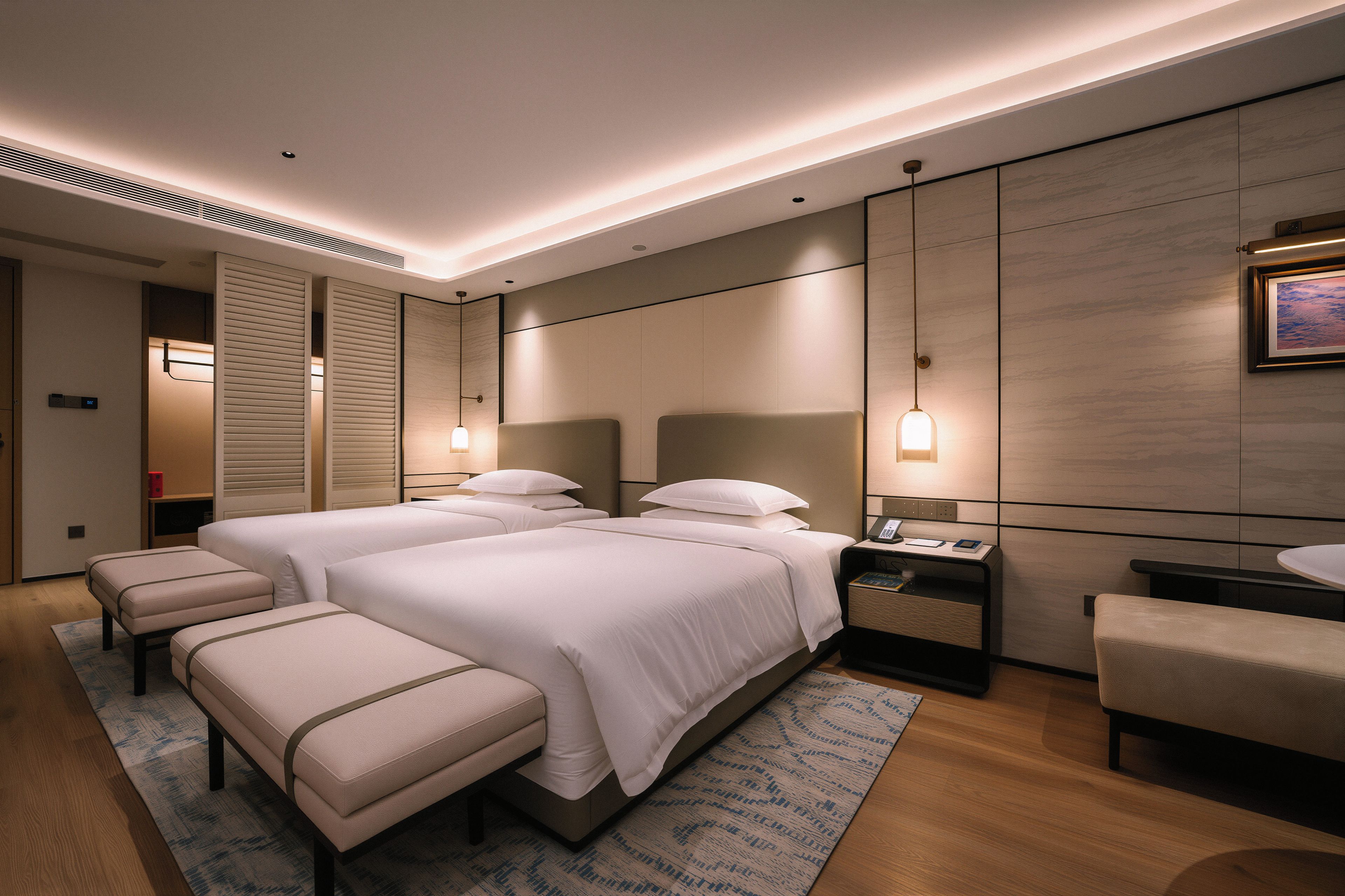 A hotel room with a large bed, two bedside tables, a desk, a chair, and a small bench.