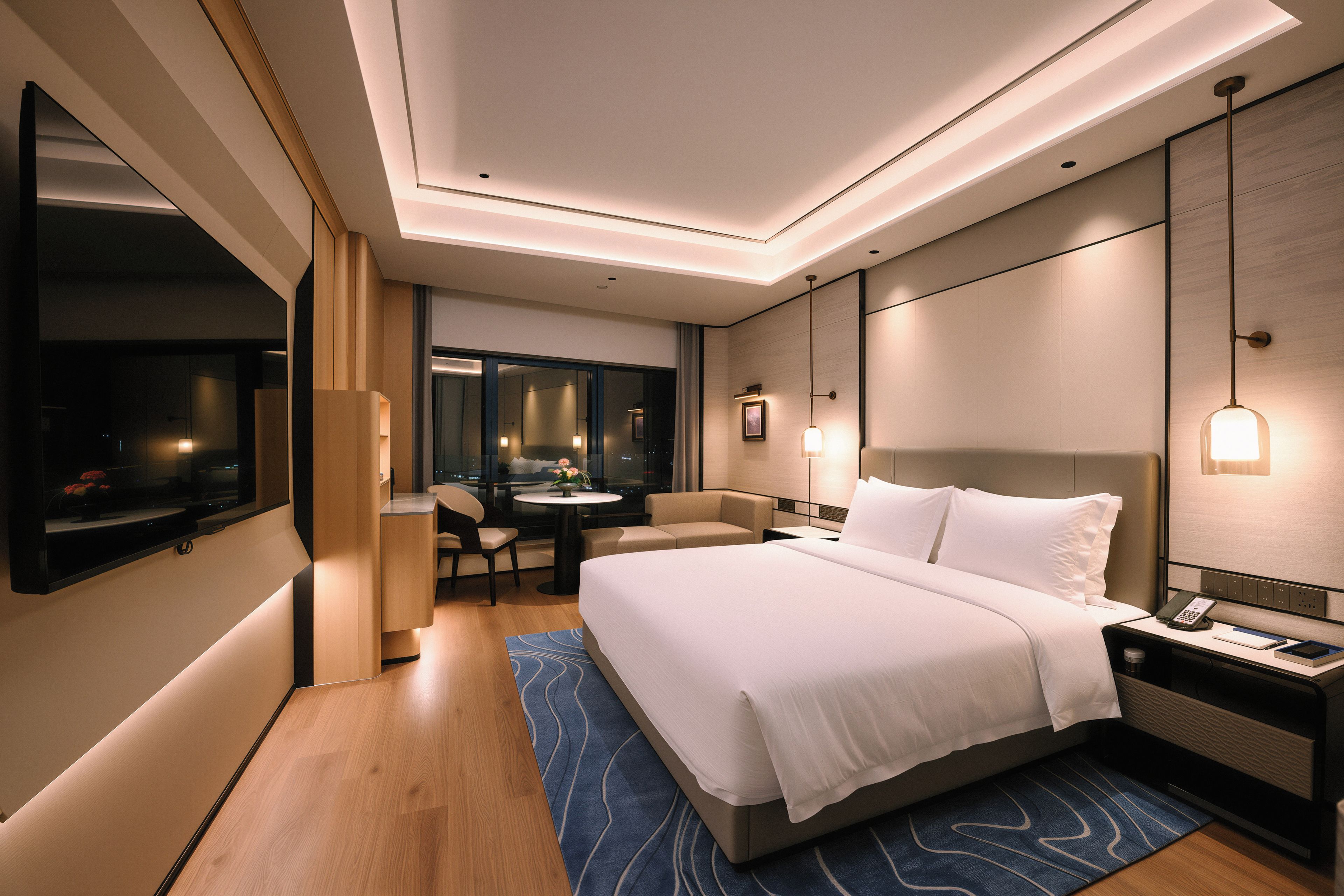 A modern hotel room with a large bed, a desk with a phone, and a seating area with a table and chairs.
