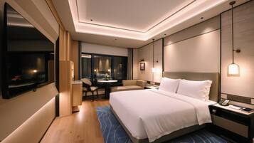 A modern hotel room with a large bed, a desk with a phone, and a seating area with a table and chairs.