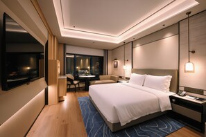 A modern hotel room with a large bed, a desk with a phone, and a seating area with a table and chairs.