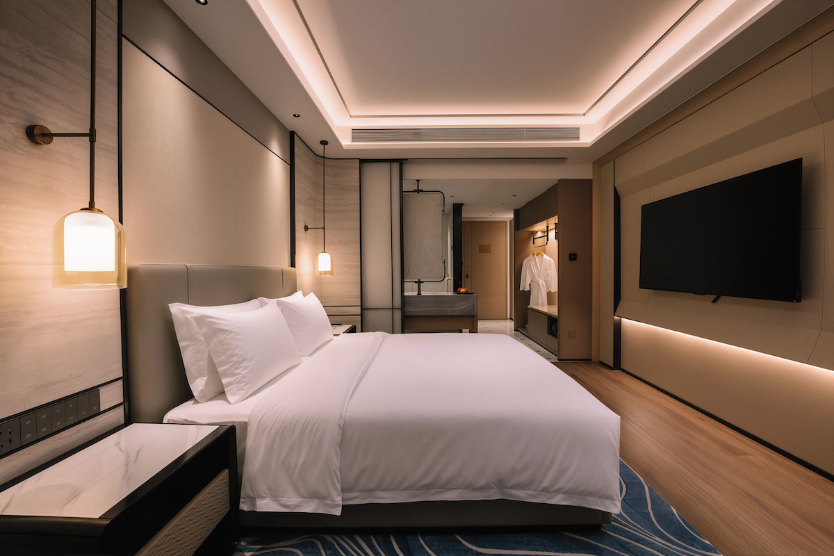 A modern hotel room with a large bed, bedside tables, a flat-screen TV, and a mirror.