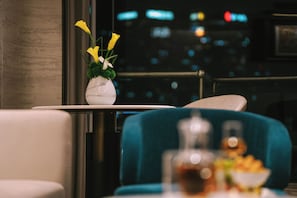 Uma área de refeições com mesa, cadeiras, um vaso com flores e vista para a cidade.