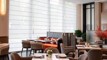 A modern dining area with a large window, a seating arrangement, and a decorative plant.