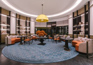 Un hall d’entrée moderne avec un espace salon central, un grand lustre et une moquette à motifs.