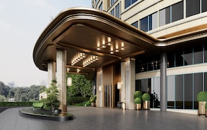 A modern hotel entrance with a covered area, large windows, and a landscaped garden.
