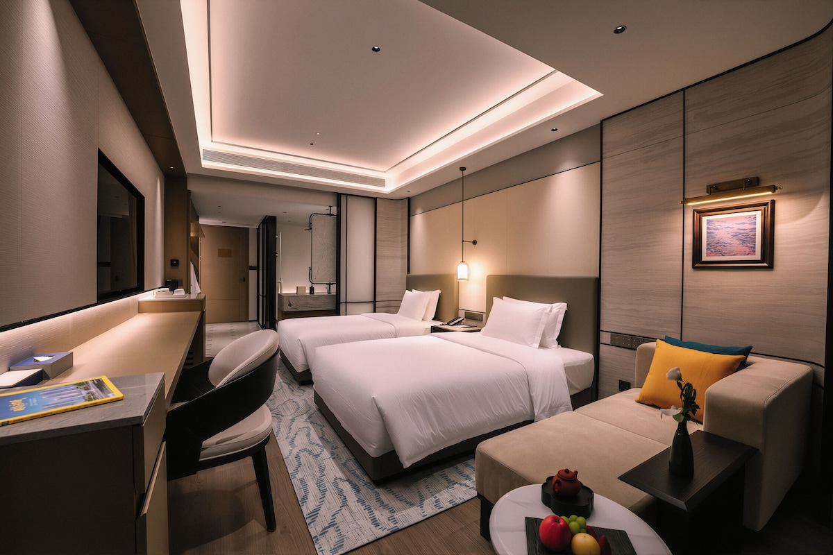 A modern hotel room with a large bed, a desk, a sofa, and a dining table.