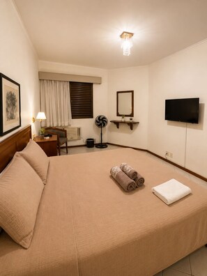 A hotel room with a large bed, a desk, a chair, a fan, a TV, and a ceiling light. - Apartment with Pool + Free Garage | Optional Coffee (Campinas)