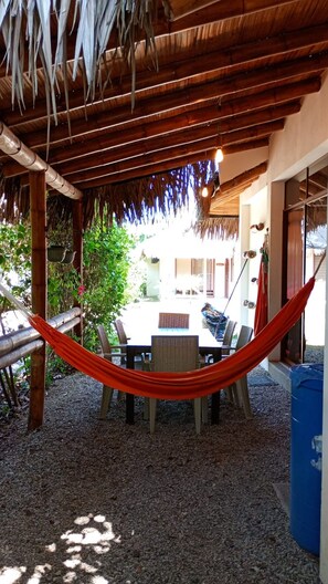 Un espace extérieur aménagé avec une table et des chaises, un hamac et une structure dotée d’un toit de chaume.