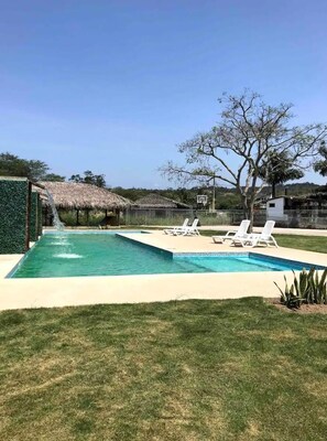 A swimming pool with a waterfall feature, surrounded by a grassy area and a few lounge chairs.