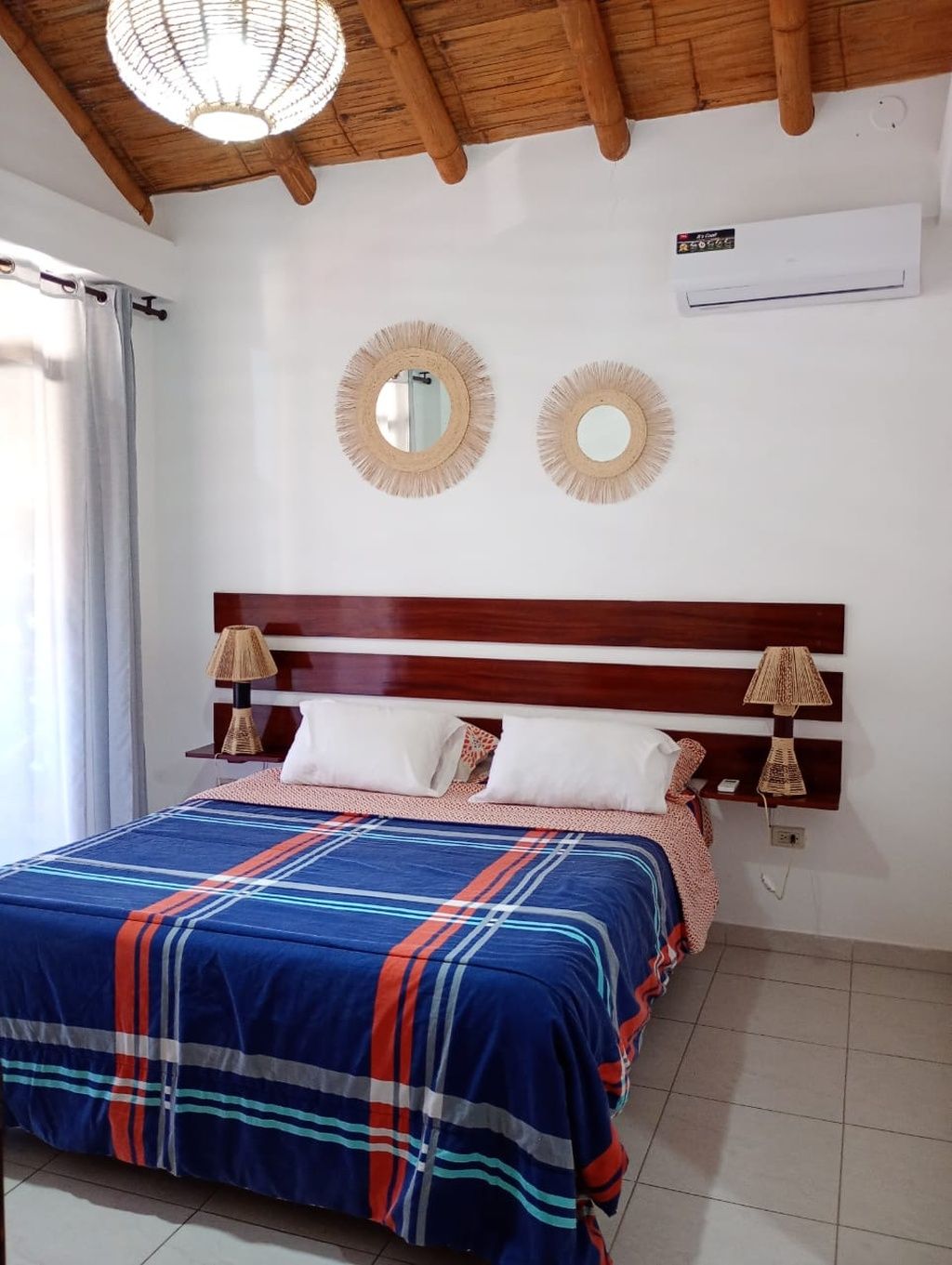 A bedroom with a wooden headboard, two wall-mounted mirrors, a bed with a striped bedspread, and two bedside lamps.