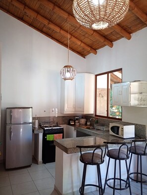 Cucina con frigorifero in acciaio inossidabile, piano cottura, forno a microonde e angolo bar con sgabelli.