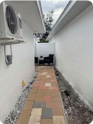 A narrow outdoor pathway with a white wall on one side and a white fence on the other. There are two chairs and a small table in the center. - Modern Private Suite Pet Friendly,Near Busch Gardens (Tampa)