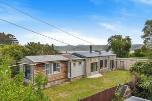A residential property with a detached house and a smaller attached structure, surrounded by a fenced yard and lush greenery.