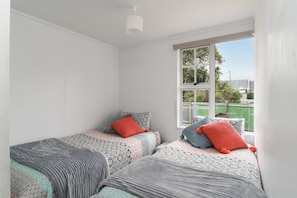 Een kamer met twee bedden, elk voorzien van beddengoed met een patroon en rode kussens, een raam met uitzicht op groen, en een witte plafondlamp.