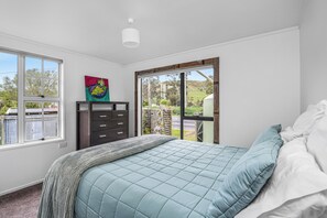 A bedroom with a bed, a dresser, a window, and a painting.